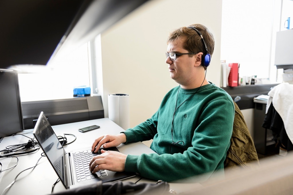 A man wearing glasses is sitting at a desk and working on a laptop